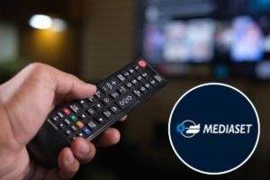 telecomando in mano puntato alla TV e logo Mediaset