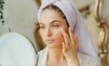 Donna con sciugamano sulla testa che mette crema viso