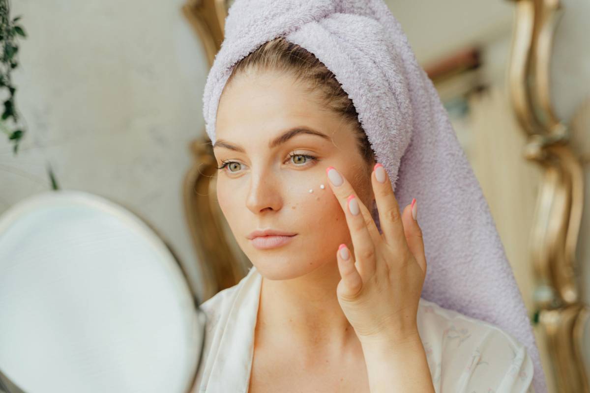 Donna con sciugamano sulla testa che mette crema viso