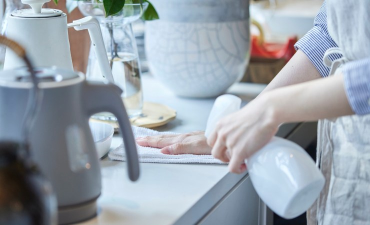 Donna che pulisce con prodotto spray mobile della cucina